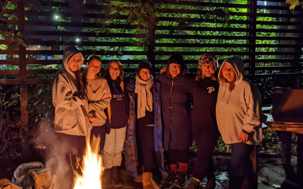 Seven of our colleagues and partners stand around the fire in warm clothes as part of the Sleep Out to Help Out fundraiser