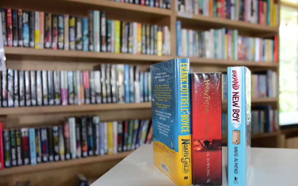 Three books stood up on a table, with a filled bookshelf behind