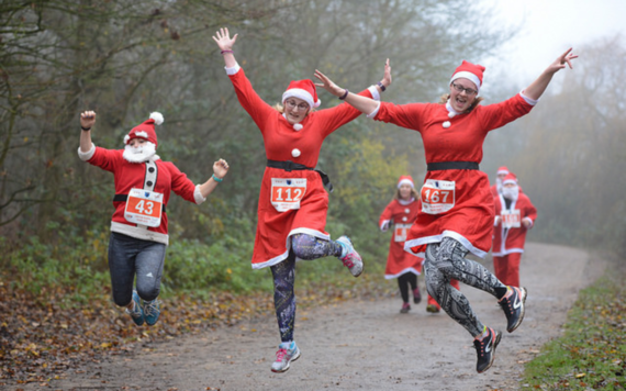 Three people dressed in Santa outfits jump as they run around Dinton Pastures on a frosty morning