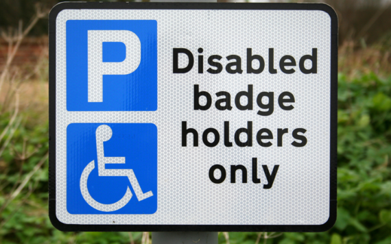 Street sign with a blue P and wheelchair logo reading disabled badge holders only