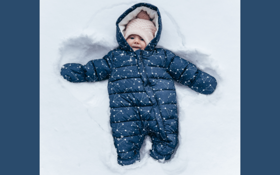 A baby in a thick snow suit and woolly hat laying on the snow 