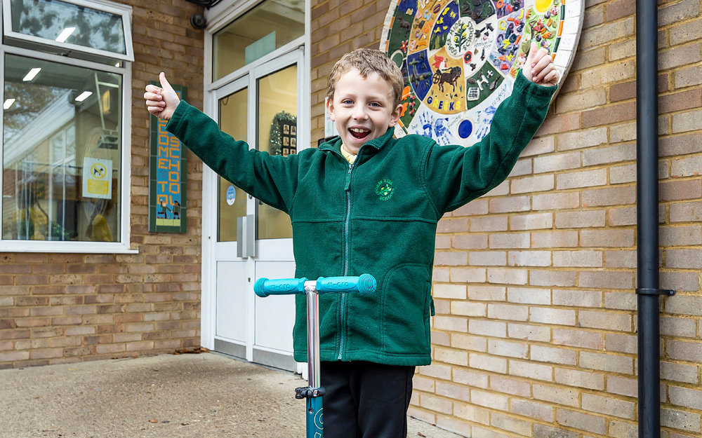 Harvey, a year four student, raises his arms aloft with his new scooter outside Gorse Ride Junior School