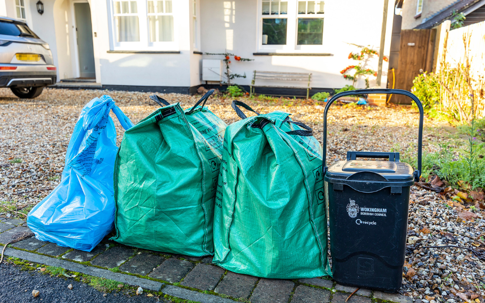 A blue waste bag, two grene recycling bags and a food waste caddy outside a house awaiting collection