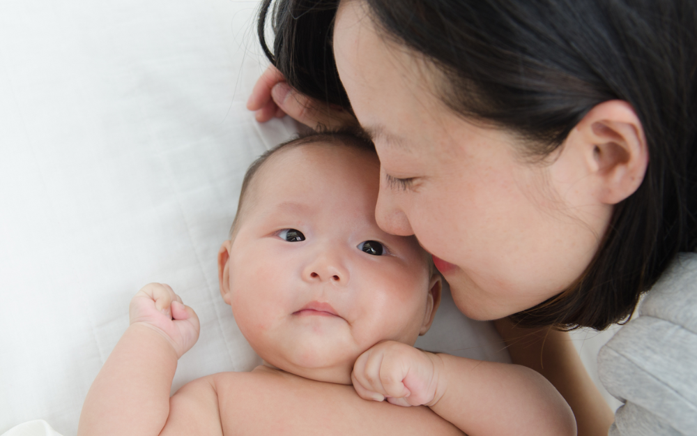 A mother holds her head closely to her child, who is laying on a white sheet