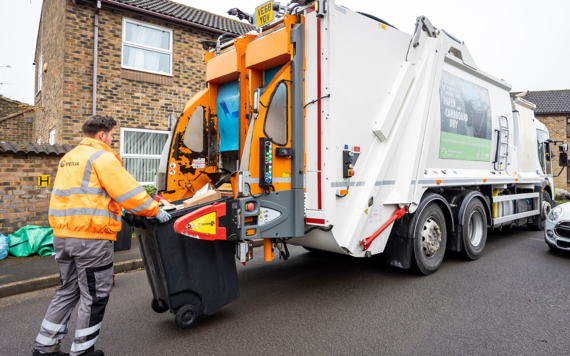A crew member pushing a wheeled bin of rubbish to a waste vehicle