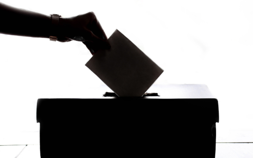 A ballot being placed in a ballot box by a hand