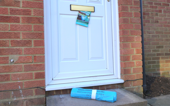 A leaflet hanging from the letterbox and a roll of blue rubbish bags on doorstep