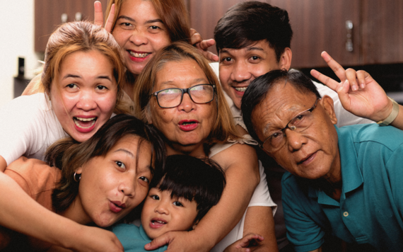 Photo of family members huddling happily together for a picture, with different generations from children through to older people