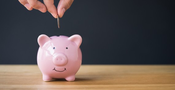 a hand putting a coin in a piggy bank