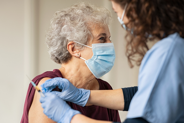 older woman wearing a face mask and receiving a covid jab