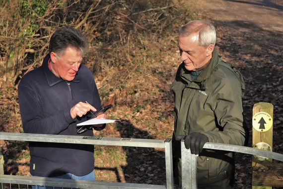 two men standing at a stile on a footpath, looking at their smartphones