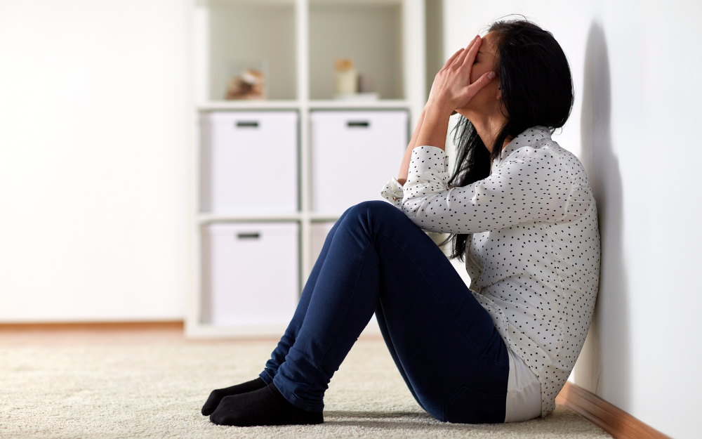 A woman holds her face in her hands while sat on the floor