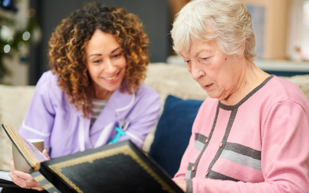 A care worker helps an older woman look through a photo album
