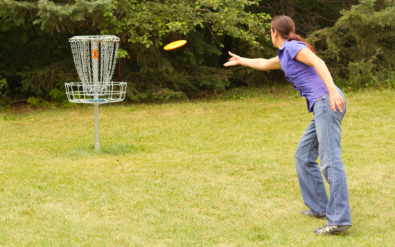 A woman throwing a frisbee disc to a basket
