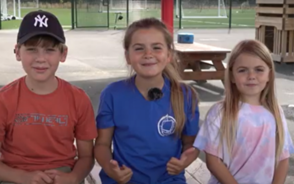Three children on playground equipment smiling into the camera