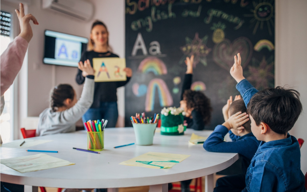 A teacher at the front of a class with a group of children watching on