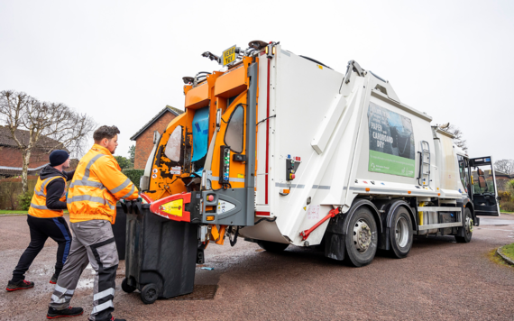 Two crews pushing wheeled bin to a waste collection vehicle