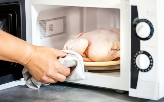 A raw whole chicken being put into a microwave for defrosting