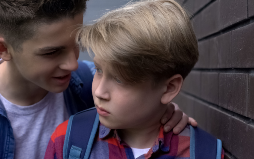 An older child whispering into the ear of a younger child