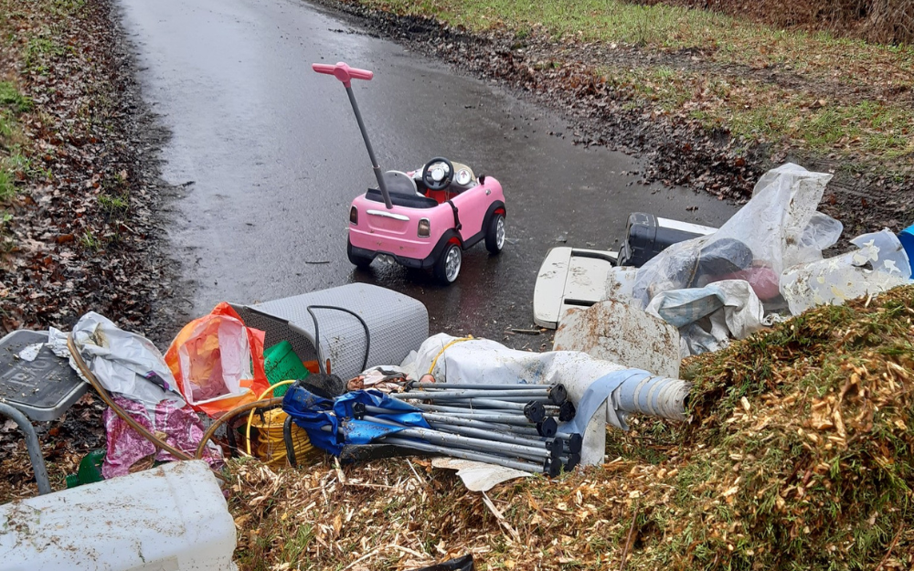 A pile of rubbish, including woodchips, garden waste and tools, and a child's ride-on toy car, completely blocking a country lane