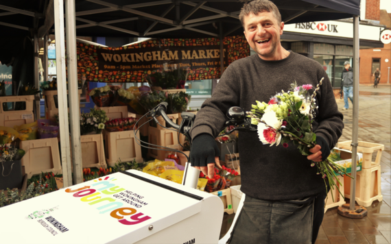 Market trader in Wokingham holding a bunch of flowers smiles while posing next to e-cargo bike
