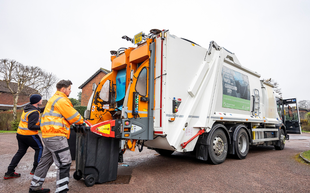 Two men put waste onto the back of a waste truck during a waste collection in Wokingham Borough