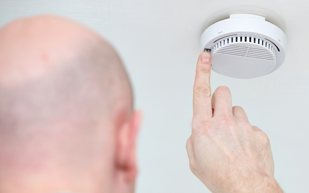 A man presses the test button on a smoke alarm on a ceiling