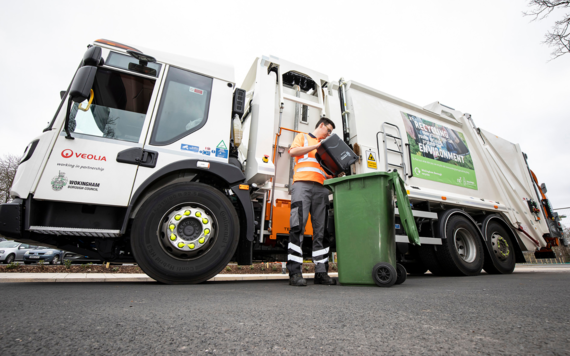 A bin collector empties a food waste caddy, standing next to a bin lorry