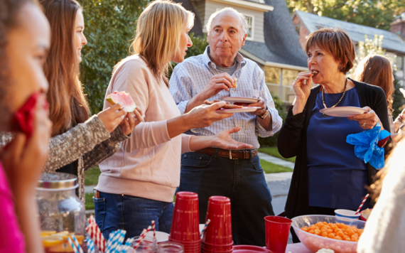 A man and two women holding paper plates with party food chat around a table at a street party