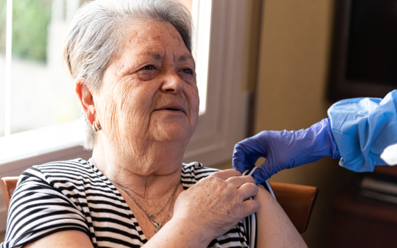 An older woman in an arm chair receives a jab in her arm