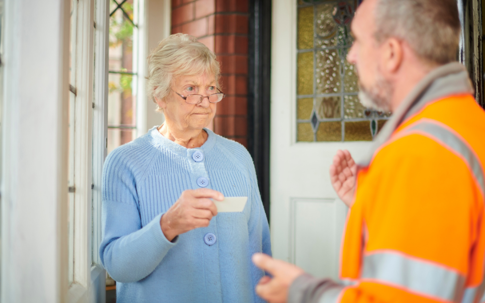 An older person inspects the ID of a workman who has come to her door