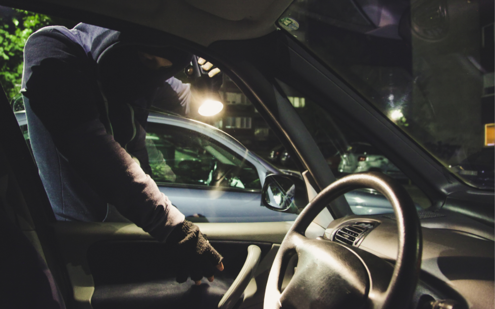 Person in a balaclava and with a torch looks into a car 