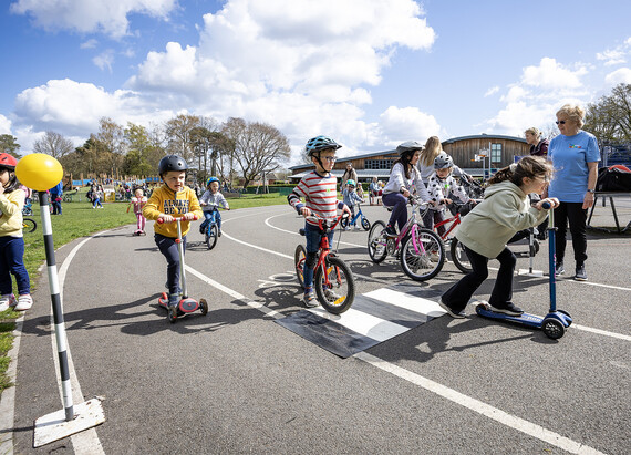 Children on bikes and scooters play on a mock-up of a road