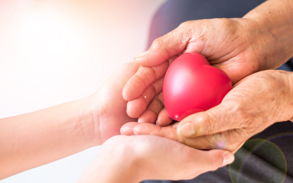 Two sets of hands clasped together, a heart shape sits on top of them