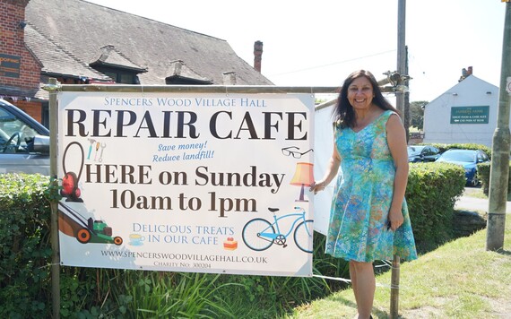 Billie Bachra who organise the Spencers Wood Village Hall repair cafe post next to a banner that reads repair cafe 