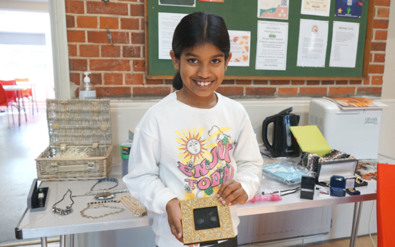 A girl holding a photo frame in front of a table with donated items