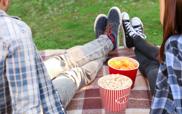 Two people sitting on a picnic rug with popcorn buckets