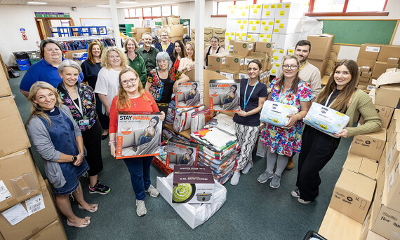 A large group of people standing in a school classroom filled with boxes of energy efficient electrical goods