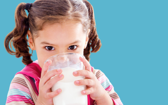 A young girl drinking a large glass of milk