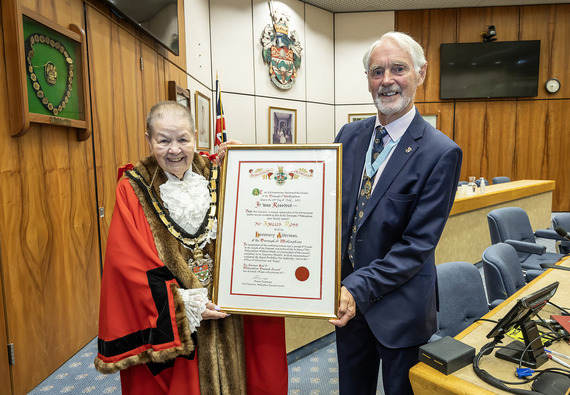 The Mayor in ceremonial robes presents an elaborate hand-written scroll to an older gentleman wearing a smart suit