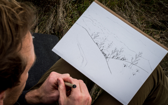 A man draws a landscape on a pad of paper