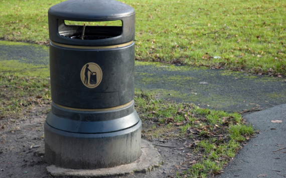 A litter bin in next to a path in a green space