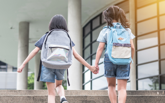 A photo showing the back of two girls going to school hand in hand