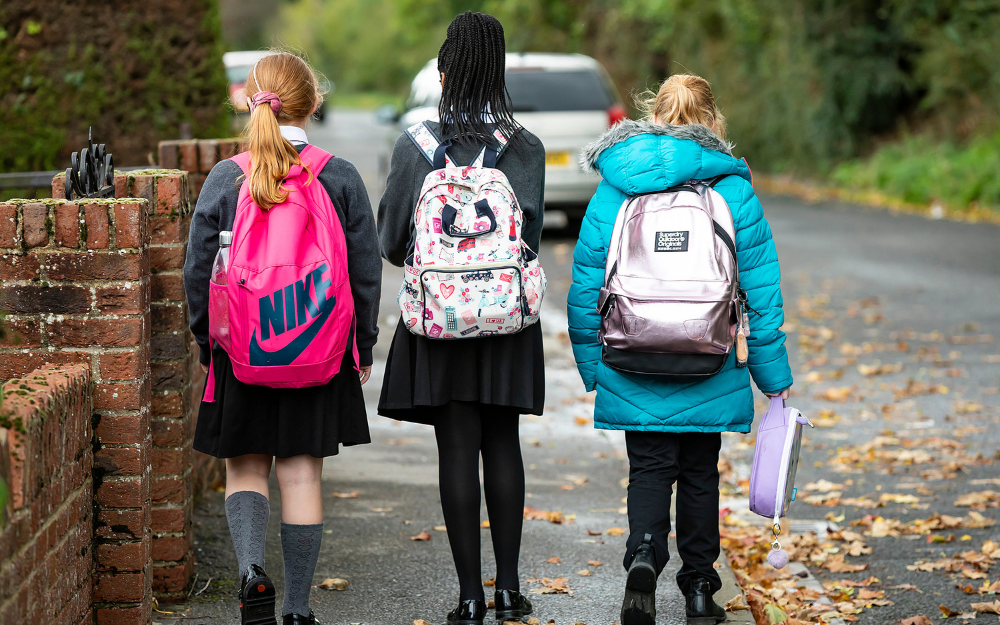 Three children walking away from the camera in their school uniform