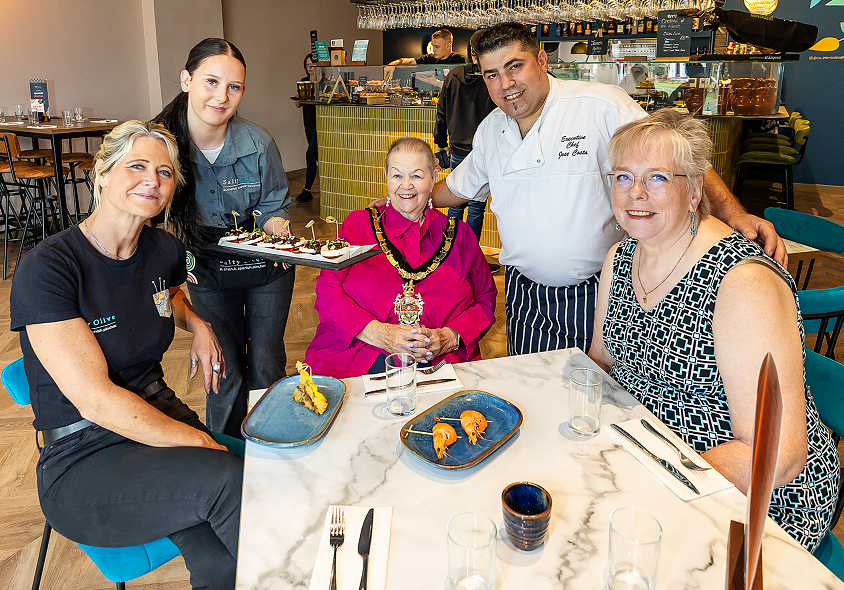 A group of people smile while sitting down and being served plates of food at a table