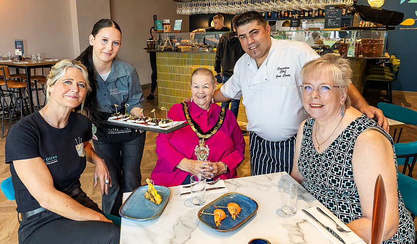 A group of people sitting around a table and smiling while being served small plates of food