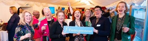 A group of women smiling and celebrating while holding a banner advertising a campaign