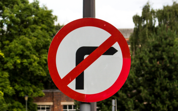 No right turn road sign mounted on a post with blurred trees and buildings in background