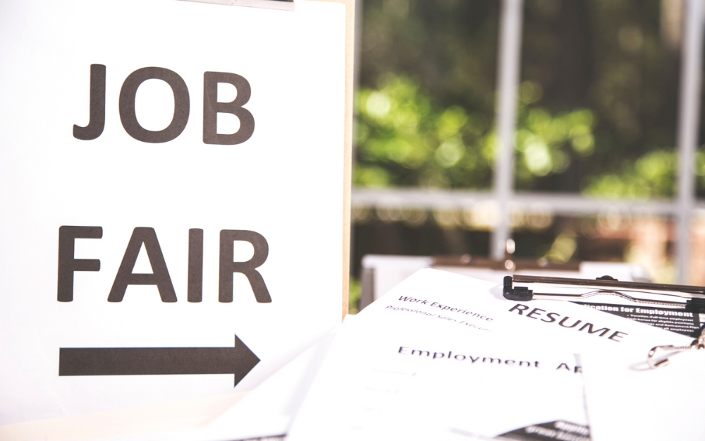 A sign which reads 'job fair', with a pile or CVs and other materials next to it