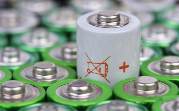 A close-up of the top of some batteries. In the middle is a battery with a symbol of a crossed out wheeled bin